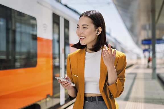Woman standing on the platform with wireless headphones and a mobile phone in her hand.