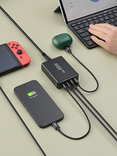 Auf einem Tisch liegen ein geöffneter Laptop, Smartphone, Nintendo Switch und Bluetooth-Kopfhörer. Sie werden alle gleichzeitig über die Hama Ladestation geladen.